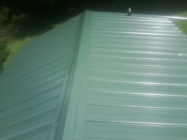 New green metal panels meeting at the ridge of a roof — Flat Roof Repair work by our crew in Mackay