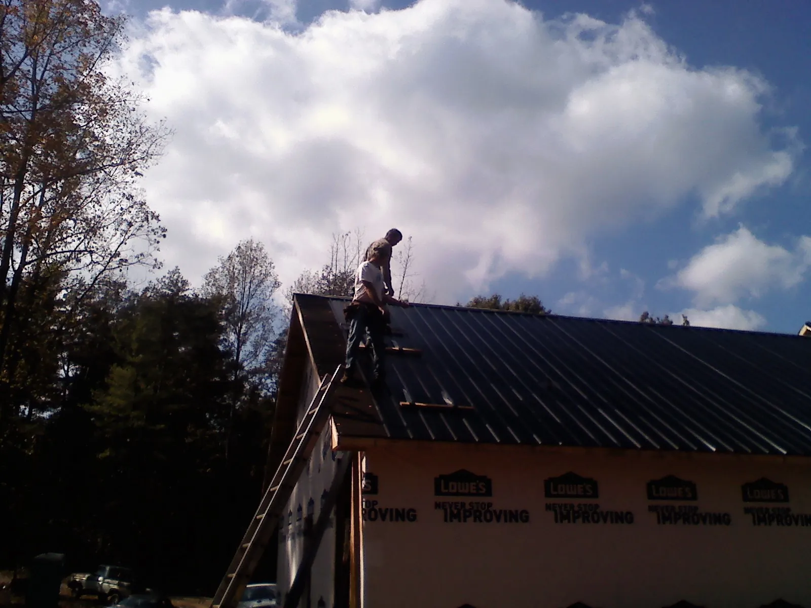 Roofer fastening dark metal panels high against a cloudy sky, from a Roof Inspection job in Mackay